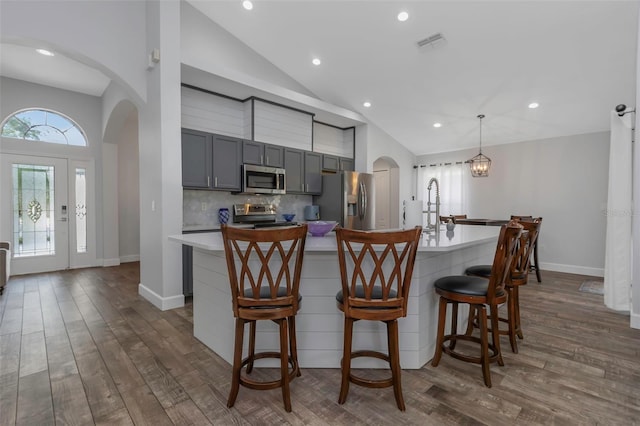 kitchen featuring appliances with stainless steel finishes, light countertops, arched walkways, a kitchen island with sink, and visible vents