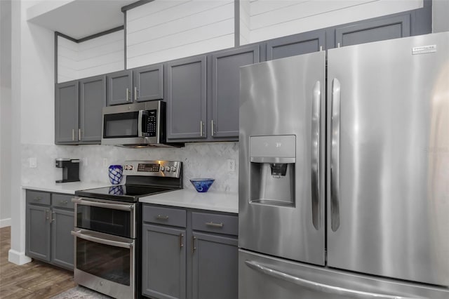 kitchen featuring appliances with stainless steel finishes, tasteful backsplash, wood finished floors, gray cabinetry, and light countertops