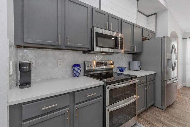 kitchen with light countertops, gray cabinets, tasteful backsplash, light wood-style flooring, and appliances with stainless steel finishes
