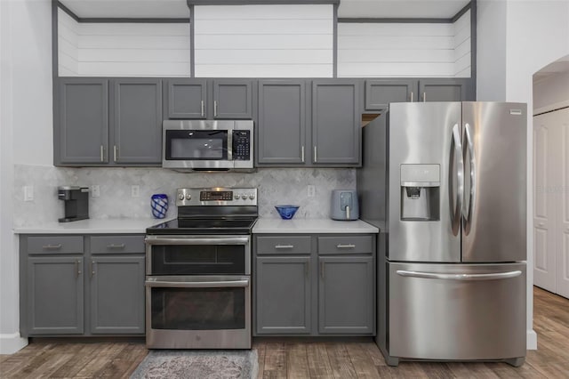 kitchen featuring light countertops, gray cabinets, stainless steel appliances, wood finished floors, and tasteful backsplash