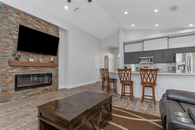 living room with visible vents, wood finished floors, a fireplace, high vaulted ceiling, and arched walkways