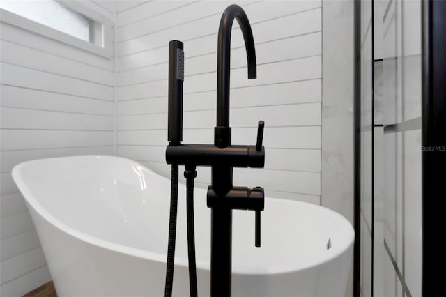 interior details featuring a sink, a freestanding tub, and wood walls