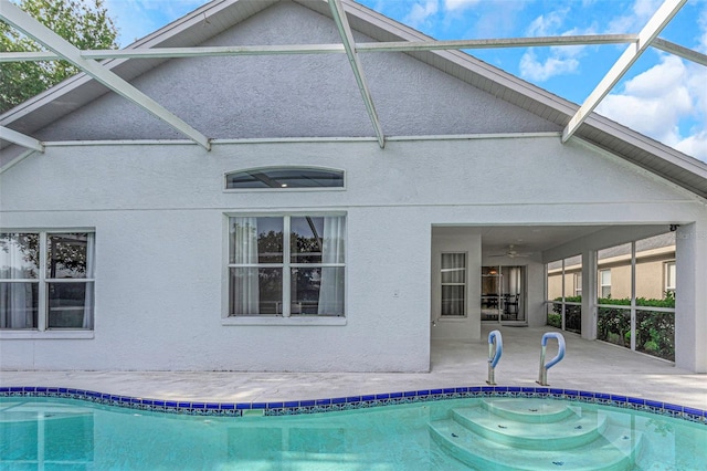 rear view of property with a lanai, stucco siding, a patio area, and an outdoor pool