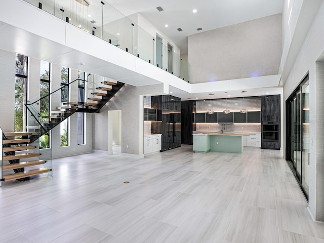 unfurnished living room with recessed lighting, stairway, a high ceiling, and visible vents