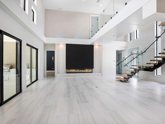 unfurnished living room with a healthy amount of sunlight, visible vents, a high ceiling, stairs, and a fireplace