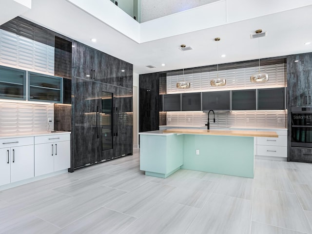 kitchen featuring modern cabinets, white cabinets, a kitchen island with sink, and decorative light fixtures