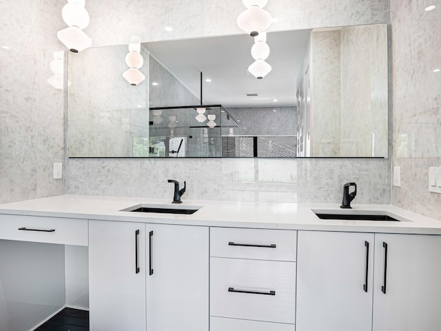 full bath with a tile shower, a sink, double vanity, and tile walls