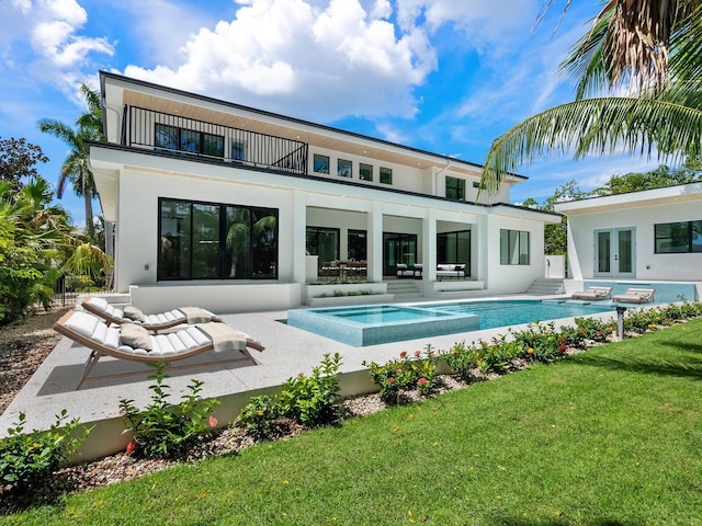 rear view of house with french doors, an in ground hot tub, a lawn, a balcony, and an outdoor pool