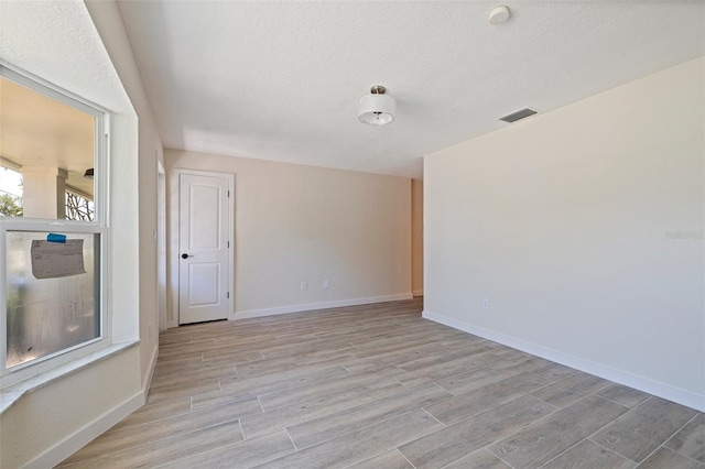 empty room with baseboards, a textured ceiling, visible vents, and light wood-type flooring