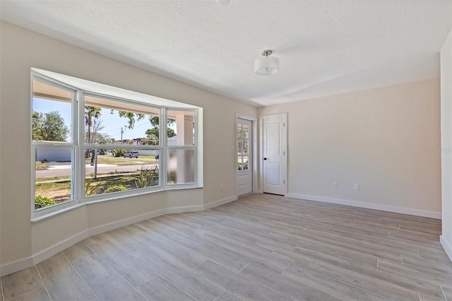 empty room with light wood-style floors, a textured ceiling, and baseboards