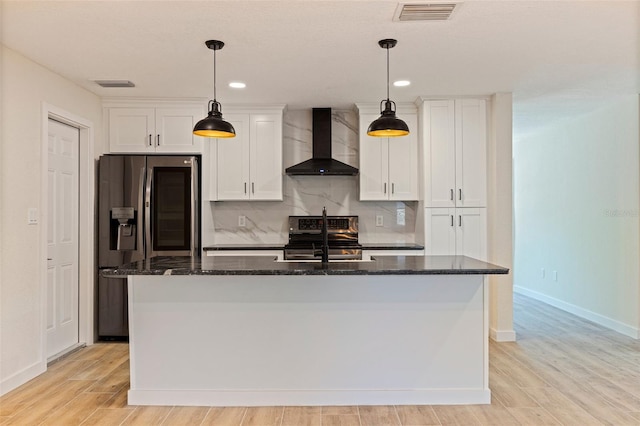 kitchen featuring appliances with stainless steel finishes, a center island with sink, wall chimney exhaust hood, white cabinetry, and visible vents