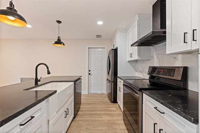 kitchen featuring wall chimney range hood, visible vents, light wood-type flooring, appliances with stainless steel finishes, and white cabinetry