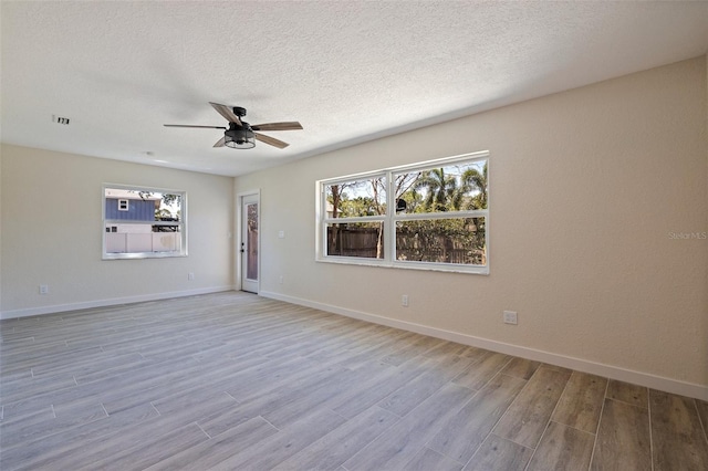 unfurnished room featuring visible vents, a ceiling fan, light wood-type flooring, baseboards, and a textured ceiling