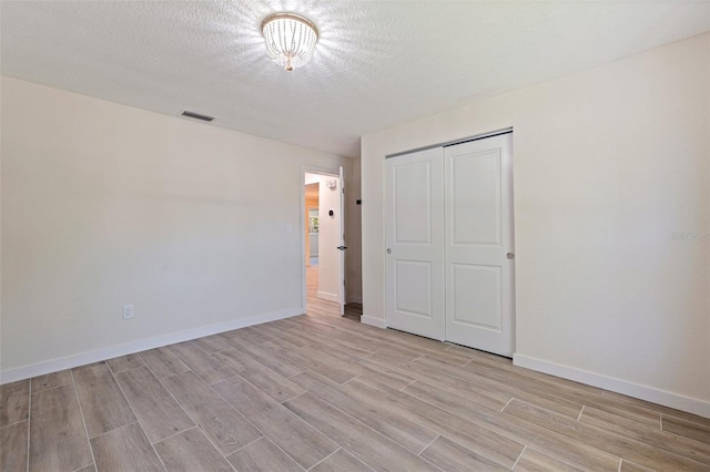 unfurnished bedroom featuring light wood-style flooring, a textured ceiling, baseboards, visible vents, and a closet