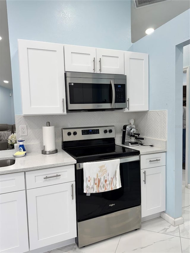 kitchen featuring backsplash, white cabinetry, appliances with stainless steel finishes, and marble finish floor