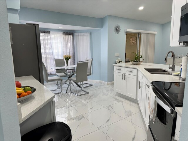 kitchen featuring electric range, a sink, marble finish floor, freestanding refrigerator, and white cabinetry