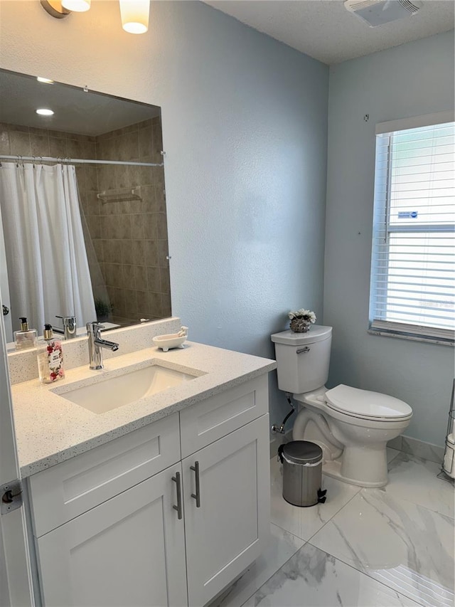 full bathroom featuring vanity, marble finish floor, toilet, baseboards, and tiled shower