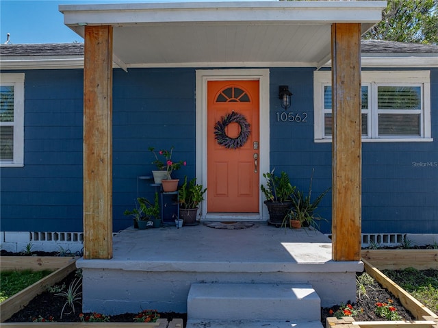 view of exterior entry with a shingled roof and covered porch