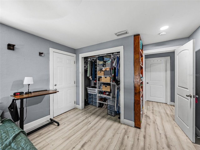 bedroom with baseboards, visible vents, wood finished floors, and a closet