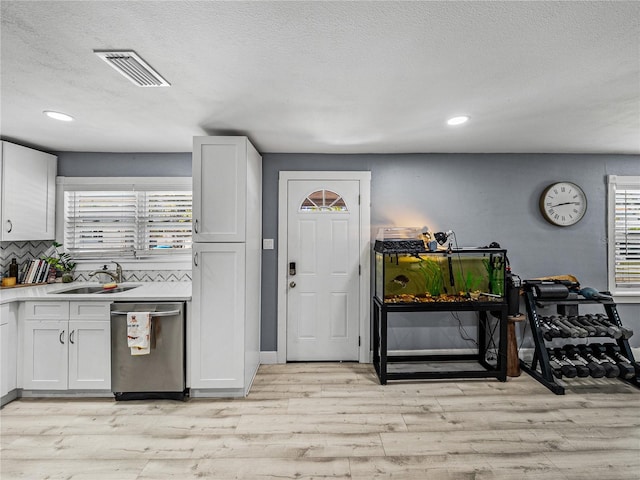 kitchen featuring light wood-style flooring, backsplash, dishwasher, a sink, and visible vents