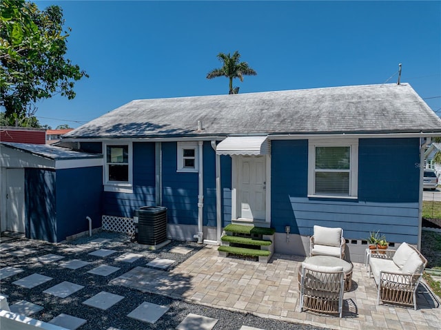 rear view of house with central air condition unit, a shingled roof, and a patio area