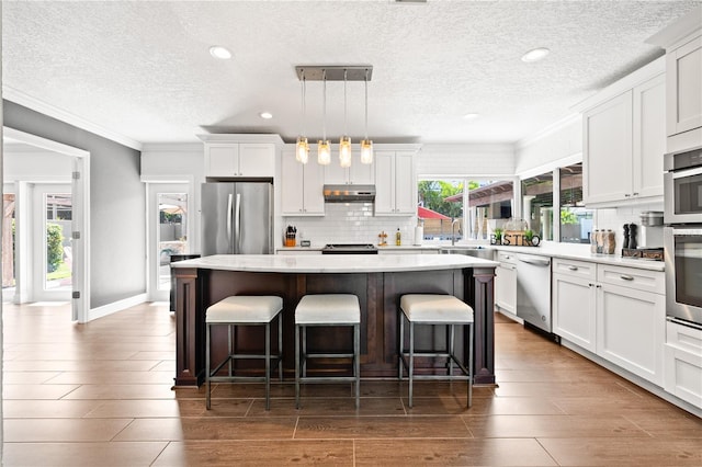 6129 Leeland St S, Saint Petersburg, FL 33715 - kitchen featuring stainless steel appliances, a textured ceiling, tasteful backsplash, under cabinet range hood, and a kitchen island