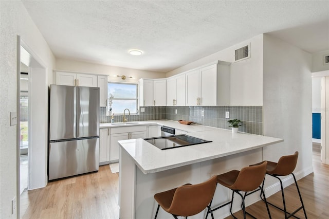 kitchen featuring stainless steel appliances, a sink, decorative backsplash, a peninsula, and a textured ceiling