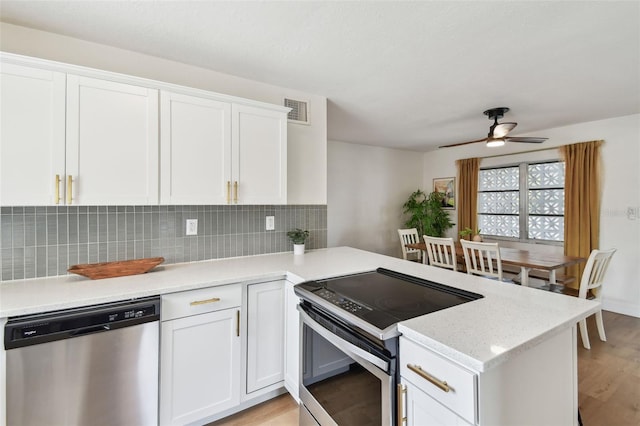 kitchen with stainless steel appliances, light wood-style flooring, a peninsula, white cabinets, and decorative backsplash