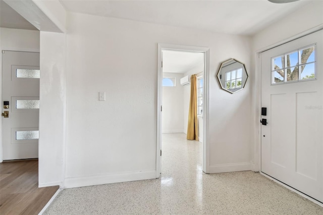 foyer entrance featuring baseboards, speckle patterned floor, and a wall unit AC