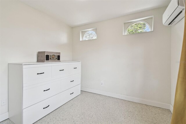 unfurnished bedroom with an AC wall unit, multiple windows, dark aggregate flooring, and baseboards