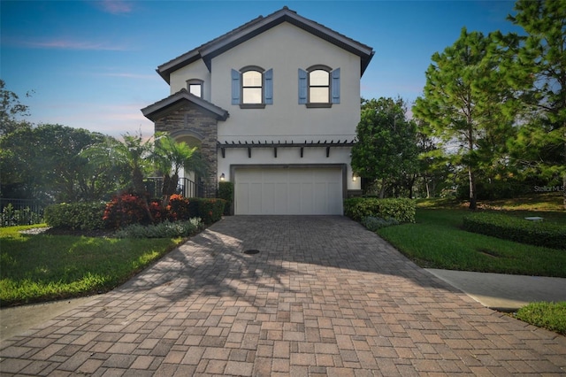 mediterranean / spanish-style home featuring a front lawn, stucco siding, an attached garage, and decorative driveway