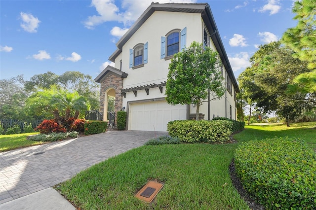 view of front of house with an attached garage, stone siding, stucco siding, a front yard, and decorative driveway