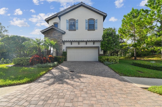mediterranean / spanish-style house with decorative driveway, a front lawn, an attached garage, stone siding, and stucco siding