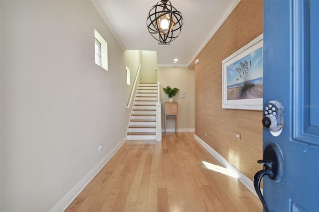 entrance foyer featuring crown molding, a notable chandelier, light wood-style flooring, baseboards, and stairway