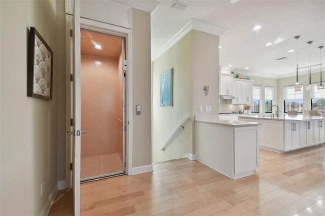 kitchen featuring crown molding, a peninsula, light countertops, white cabinets, and light wood-style flooring