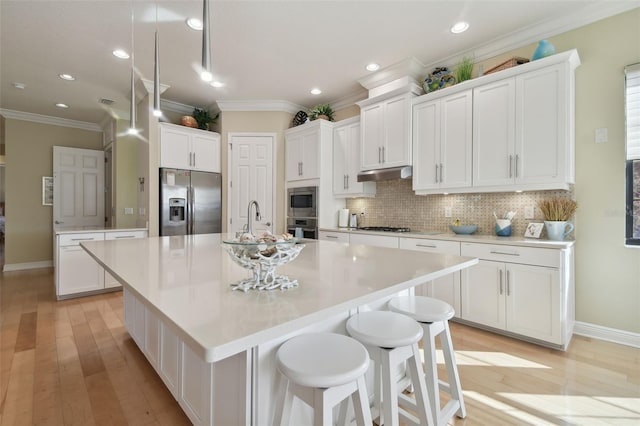 kitchen with tasteful backsplash, under cabinet range hood, ornamental molding, stainless steel appliances, and an island with sink