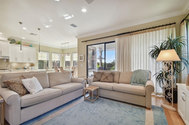 living room with ornamental molding, light wood-type flooring, and visible vents