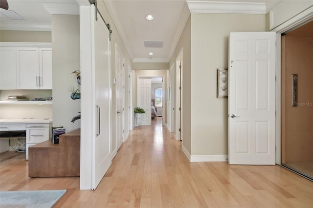 hallway with light wood-type flooring, ornamental molding, baseboards, and a barn door