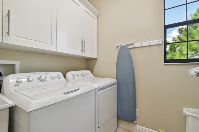 clothes washing area featuring separate washer and dryer, baseboards, and cabinet space