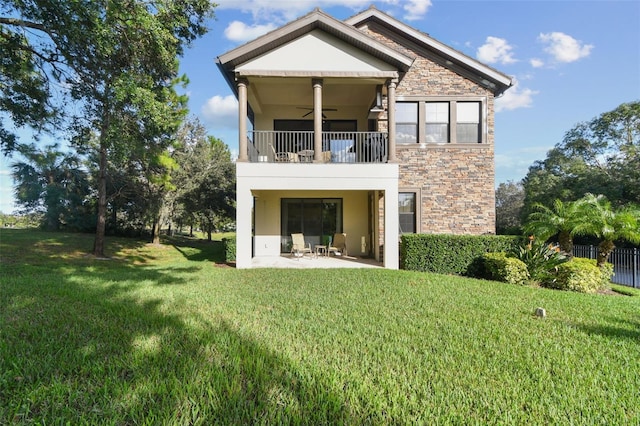 rear view of property with stone siding, ceiling fan, stucco siding, a balcony, and a lawn