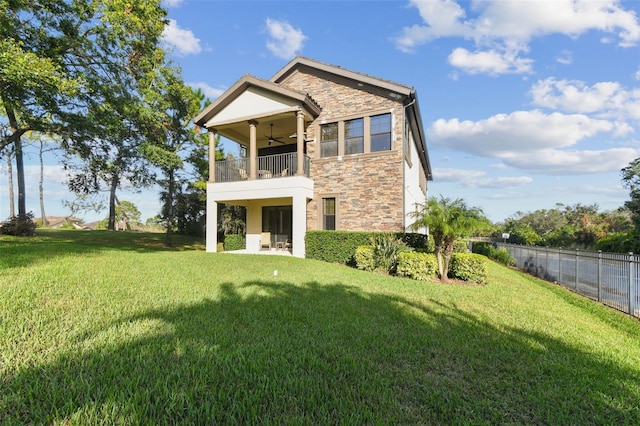 rear view of house featuring a lawn, a ceiling fan, a balcony, and stone siding