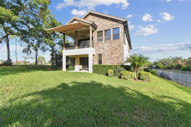 back of property with a lawn, a ceiling fan, a balcony, and stone siding