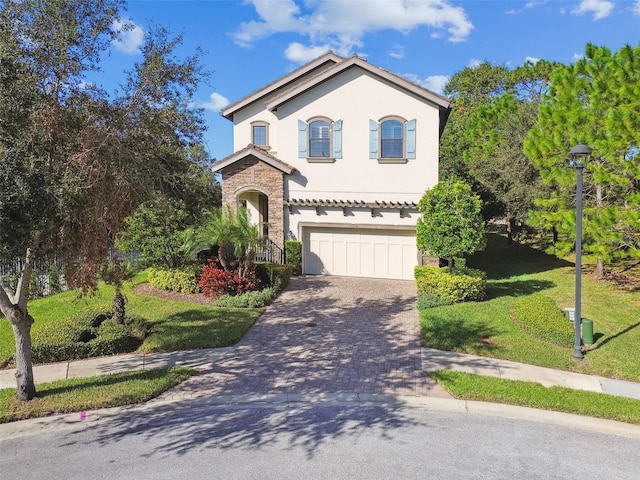 mediterranean / spanish house featuring a front lawn, stone siding, stucco siding, an attached garage, and driveway
