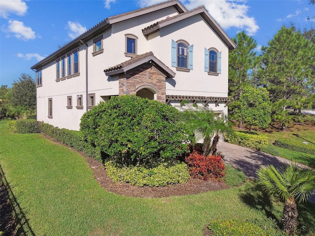 exterior space featuring driveway, a lawn, a garage, stone siding, and stucco siding