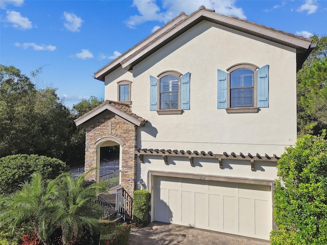 mediterranean / spanish home featuring stone siding, decorative driveway, stucco siding, an attached garage, and a tile roof