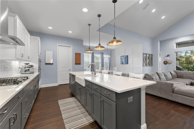 kitchen with a sink, wall chimney range hood, stainless steel appliances, white cabinetry, and open floor plan