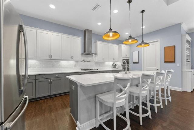 kitchen with freestanding refrigerator, wall chimney range hood, gray cabinetry, cooktop, and dark wood finished floors