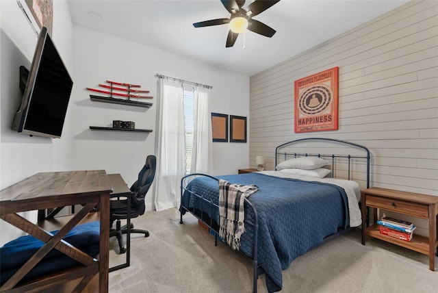 carpeted bedroom with wood walls, a ceiling fan, and a desk