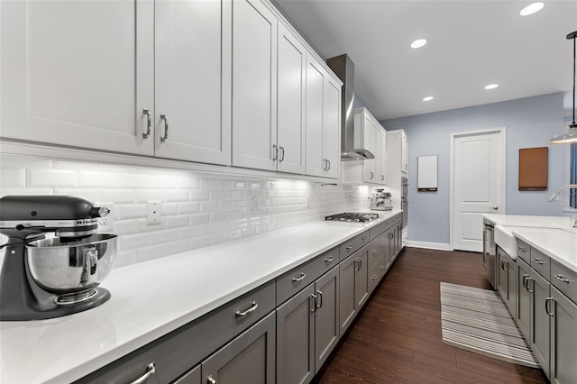 kitchen with wall chimney range hood, a sink, appliances with stainless steel finishes, gray cabinets, and tasteful backsplash