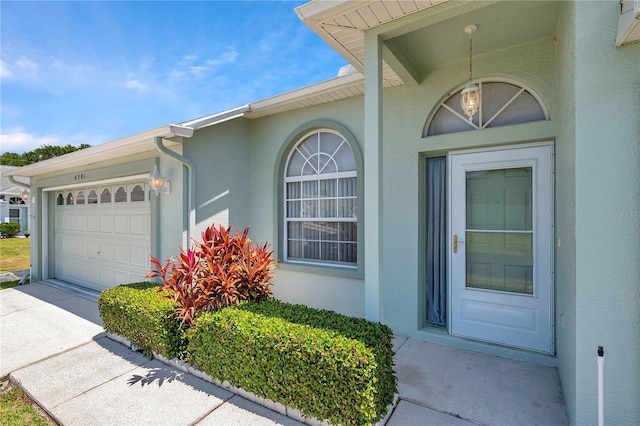 view of exterior entry with an attached garage, driveway, and stucco siding